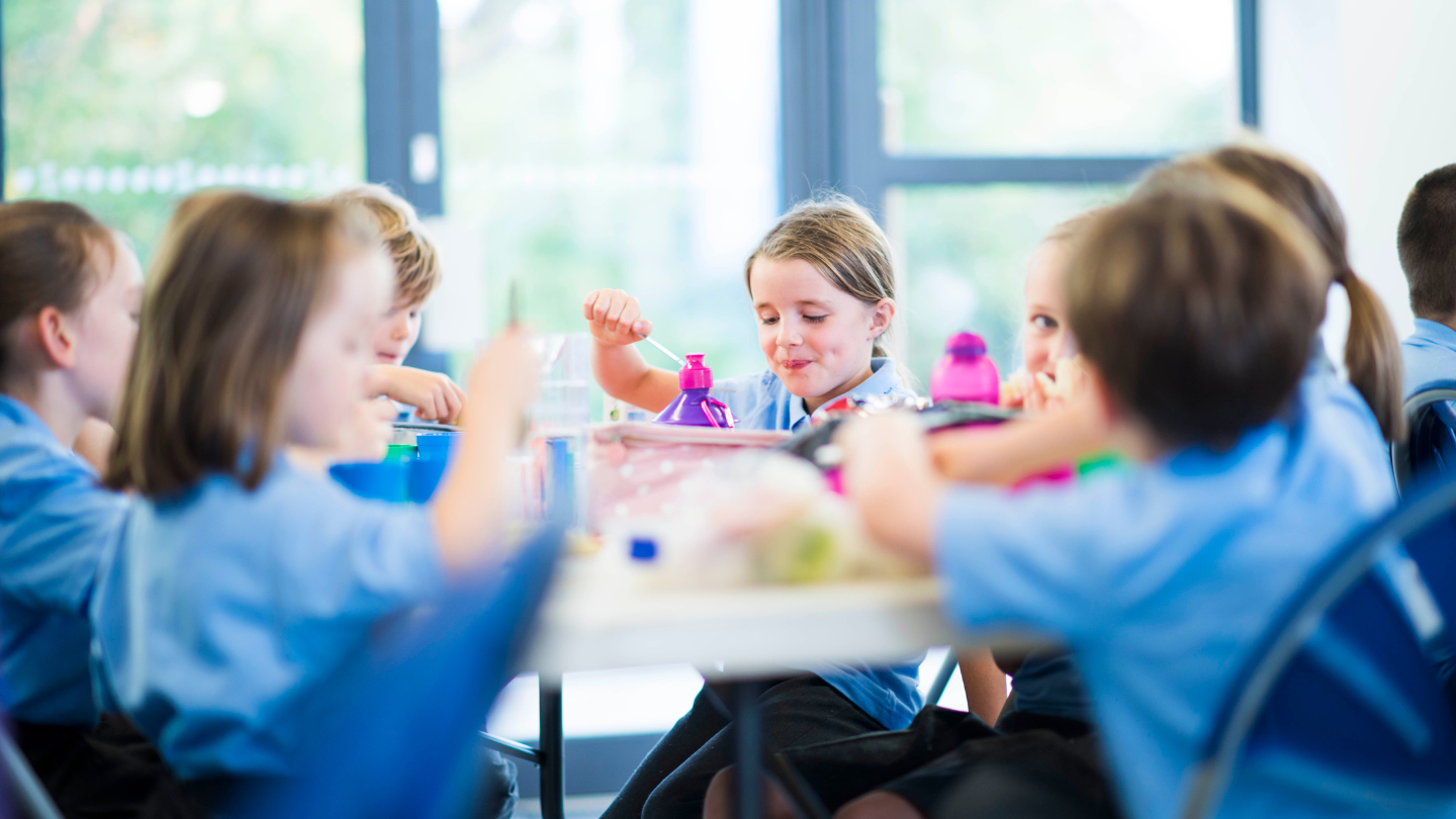 School children eat lunch in a hall on a hot day.