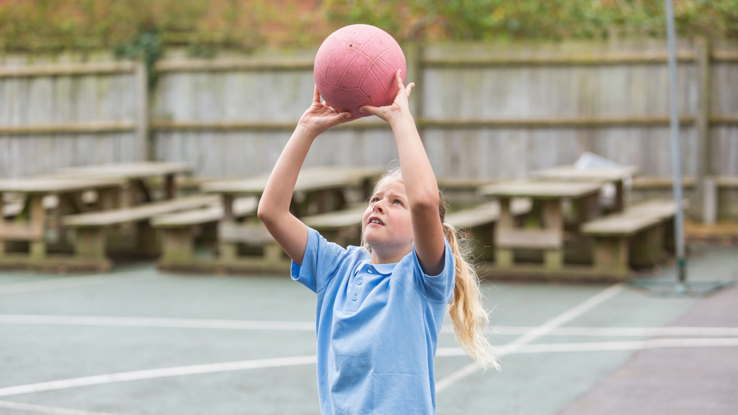 A girl plays netball in a school in the summer.